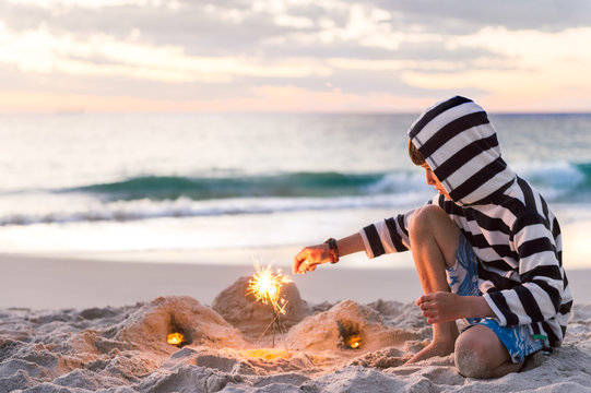Boy having fun with sparklers at the beach at sunset