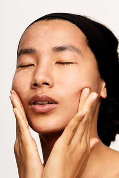 Young natural asian woman portrait applying moisturiser.