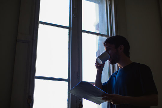 Man drinking coffee whilst reading script at home.