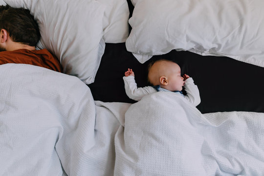 A baby boy asleep in a big bed with his Dad co-sleeping by his side