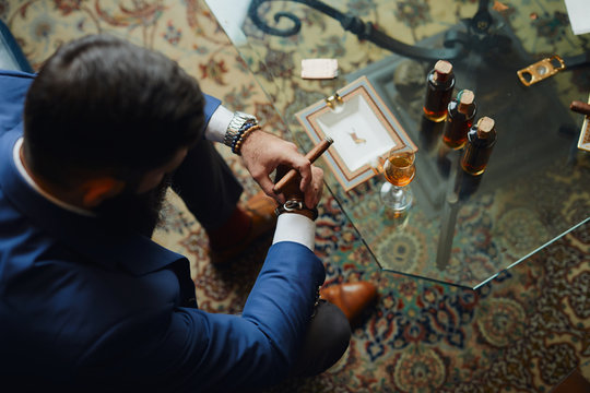 Man with beard smoking cuban cigar and drinking rum.