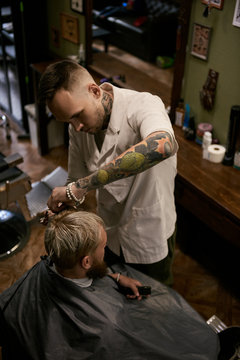 Tattooed barber giving hairstyle to man
