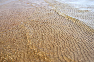 Sand texture created by sea waves on beach coast. Sand pattern under soft waves. Sand texture of Baltic sea coast.