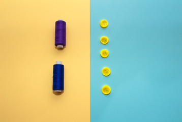 Composition with dark blue threads and sewing accessories on yellow background. Yellow buttons on blue background. Flatlay, place for text