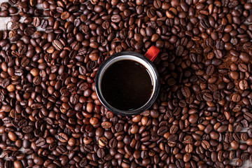 Coffee beans background with a red metal cup in the center with freshly made coffee