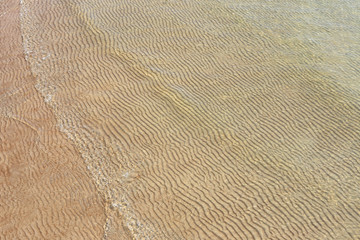 Sand texture created by sea waves on beach coast. Top view of sand pattern under soft waves. Sand texture of Baltic sea coast.