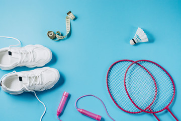 Sports flat lay with shuttlecock and badminton racket, skipping rope, sneakers and measuring tape on blue background. Fitness, sport and healthy lifestyle concept.