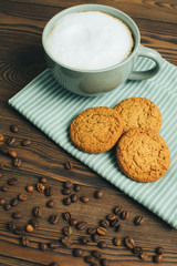Cup of coffee, cappuccino or latte with oatmeal cookies at textile and coffee beans at old wooden background