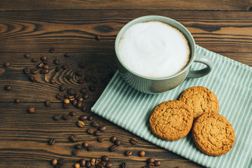 Cup of coffee, cappuccino or latte with oatmeal cookies at textile and coffee beans at old wooden background