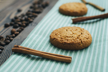 Oatmeal cookies at green kitchen textile with cinnamon sticks and coffee beans at wood background