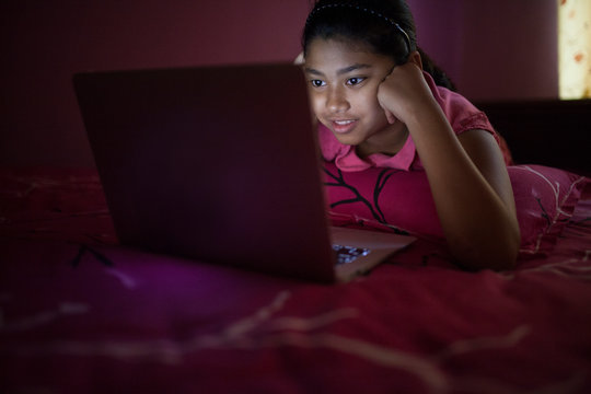 Teenage girl lying on the bed comfortably and using laptop inside a room