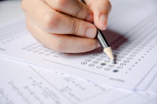 Students hand holding pencil writing selected choice on answer sheets and Mathematics question sheets. students testing doing examination. school exam