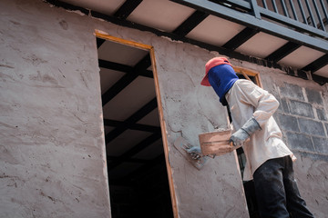 Construction workers plastering building wall using cement plaster