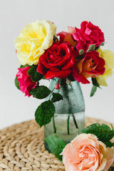 composition of colorful roses in a vase on a wicker napkin on a white background
