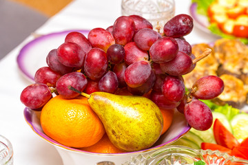 Fruit in a plate on the table. Bunch of grapes, pear and orange on the plate