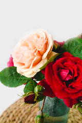 composition of colorful roses in a vase on a wicker napkin on a white background
