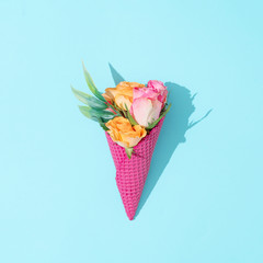 Pink ice cream cone with colorful flowers on pastel blue background. Minimal summer flat lay composition.