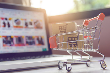 Shopping online. Parcel or cardboard boxes with a shopping cart logo in a trolley on a laptop...