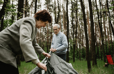 Senior couple enjoying vacation and is setting up the tent. Adults spending summer holiday on nature and pitch a tent. Seniors is camping and assembling tent