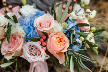 A delicate and very beautiful wedding bouquet of roses, greenery, eustoma and hydrangea on a background of dry stump. Bridal trendy florists in pastel colors. Handle decorated with pink ribbons