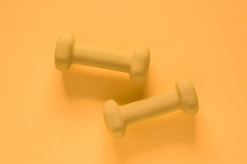 Fitness equipment with womens yellow weights/ dumbbells isolated on a yellow background with copyspace