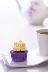 Cupcake in purple wrap and a cup of tea on white natural marble table top with copy space.