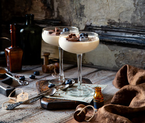 Two champagne glasses with caramel colored panna cotta, jelly, mousse or pudding with chocolate and blueberries on top stands on wooden board
