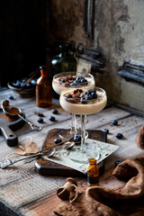 Two champagne glasses with caramel colored panna cotta, jelly, mousse or pudding with chocolate and blueberries on top stands on wooden board