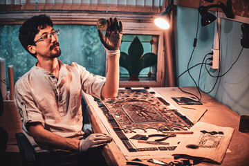 Expirienced restorer is choosing right peace of stained glass for his project at his workplace.