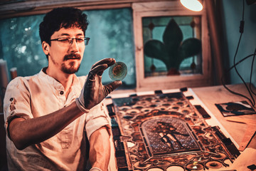 Expirienced restorer is choosing right peace of stained glass for his project at his workplace.