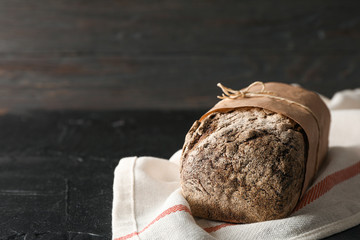 Rye bread on kitchen towel on black table against wooden background, space for text and closeup