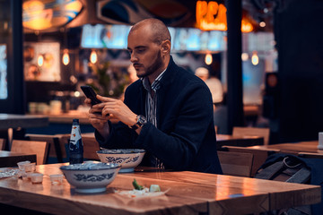 Serious sucessful businessman is chatting by mobile phone while sitting at restaurant.