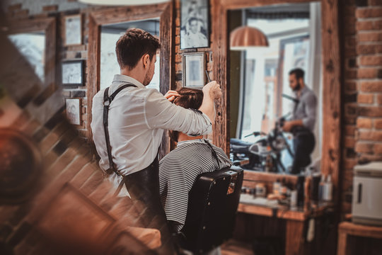 Thendy focused hairdresser at modern barbershop is working on client's haircut.