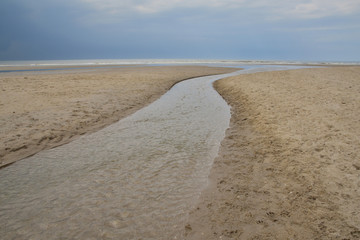 Plażą nad morzem w pochmurny dzień pod niebem z chmurami.
