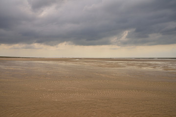 Fototapeta na wymiar Plażą nad morzem w pochmurny dzień pod niebem z chmurami.