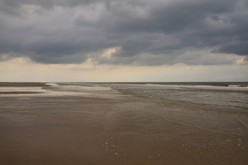 Plażą nad morzem w pochmurny dzień pod niebem z chmurami.