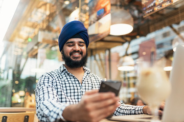 Young bearded indian man using smartphone and laptop