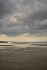 Fototapeta premium Plażą nad morzem w pochmurny dzień pod niebem z chmurami.