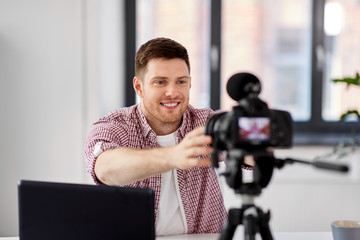 Fototapeta na wymiar blogging, videoblog and people concept - male video blogger adjusting camera at home office
