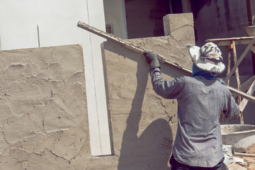 Construction workers plastering building wall using cement plaster