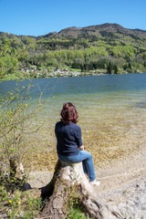 Fototapeta premium Junge Frau sitzt auf einem Baumstumpf am See