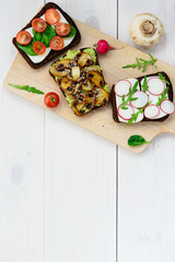 Sandwich set on a wooden board. Sandwiches radish, avocado, mushrooms, tomatoes, spinach, bread and cheese. Top view, copy space.