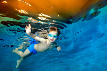A little boy swims underwater in the pool near the surface of the water. Portrait. Underwater photography. Blue background. Horizontal orientation - obrazy, fototapety, plakaty