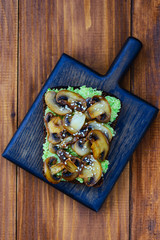 Sandwich from fried champignons, avocado and sesame on a wooden board.