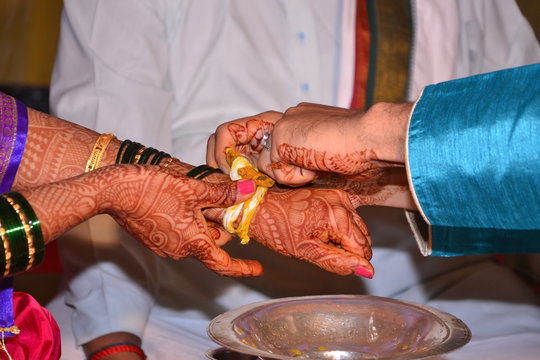Maharashtrian Wedding Ritual - Bridegroom tying kankan or halkund with thread on wrist of bride performing ritual vidhi in maharashtrian wedding ceremony