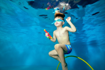 Little sports boy swims underwater,dives to the bottom of the pool for toys. Portrait. Photo underwater. Horizontal orientation