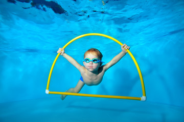 A little sports boy is engaged in swimming in the pool, underwater at the bottom, posing with a...