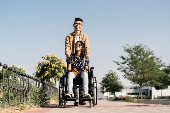 Young woman sitting on a wheelchair and her boyfriend walking