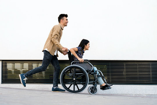 Young woman sitting on a wheelchair and her boyfriend walking very fast in the street