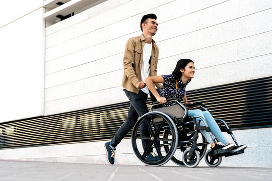 Young woman sitting on a wheelchair and her boyfriend walking very fast in the street